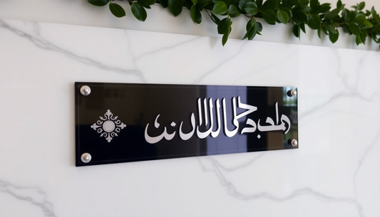 Elegant black and silver personalized home name plate ideas mounted on a white marble wall with greenery above