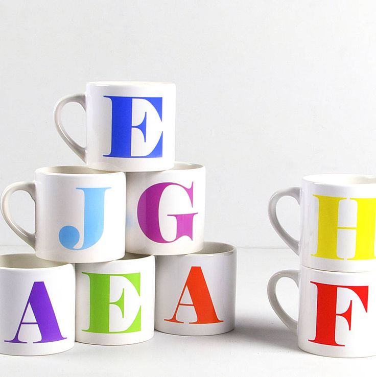 Set of white custom initial name mugs with colorful letters arranged on a white surface