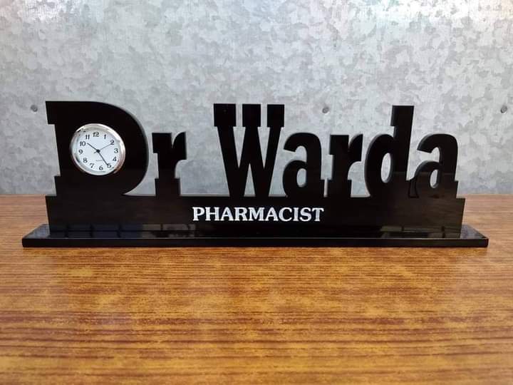 Black personalized doctor name desk clock with Dr Warda text and pharmacist title on wooden surface
