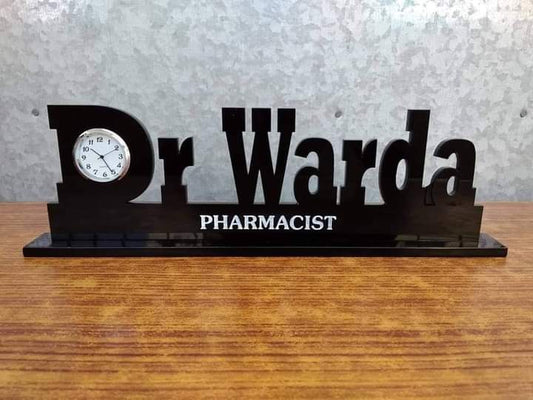 Black personalized doctor name desk clock with Dr Warda text and pharmacist title on wooden surface