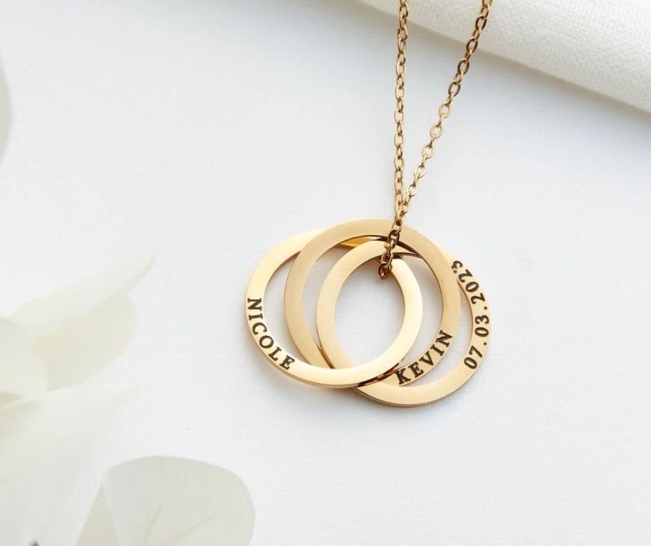 Personalized mom necklace with kids names engraved on three gold rings hanging on a gold chain