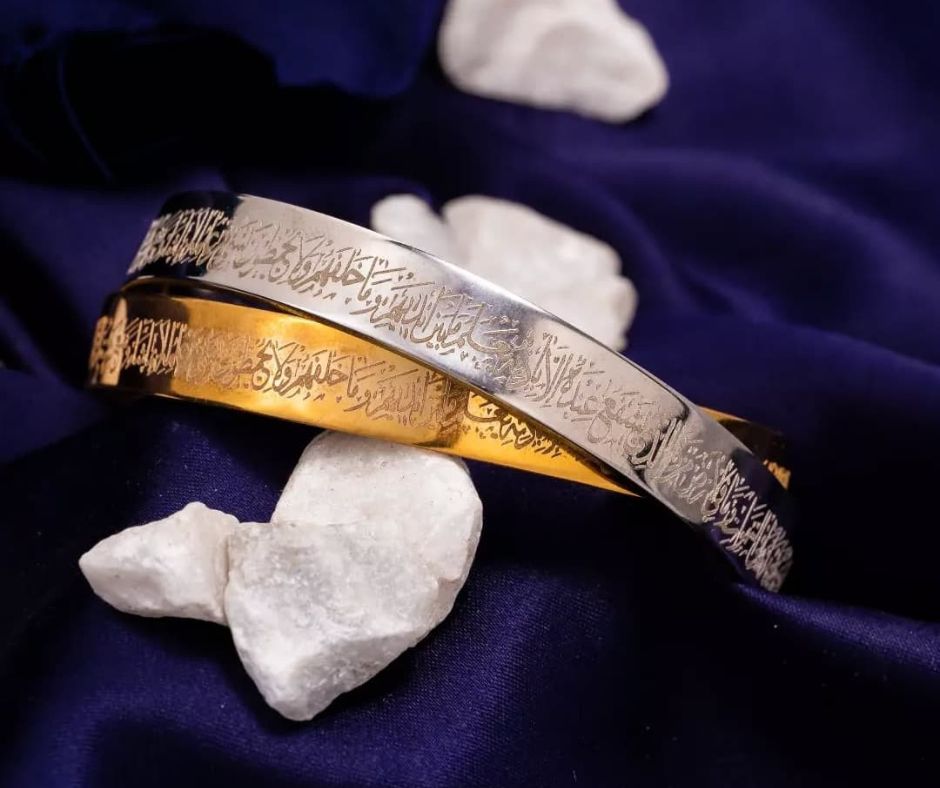 Silver and gold personalized Ayatul Kursi bangle set with intricate Arabic calligraphy on fabric background