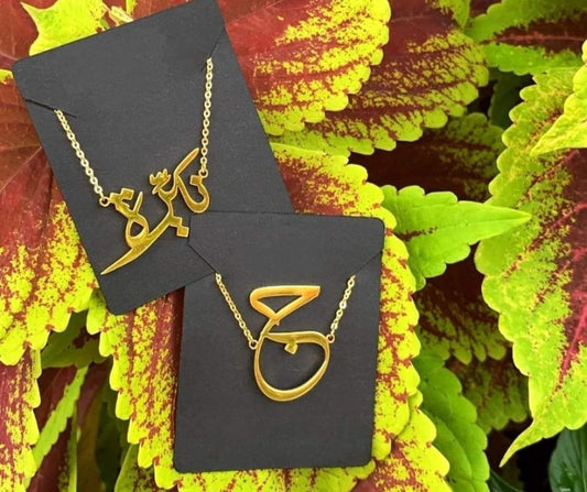 Creativegift.pk custom name necklace gold plated in Arabic script on black card with colorful leaves background