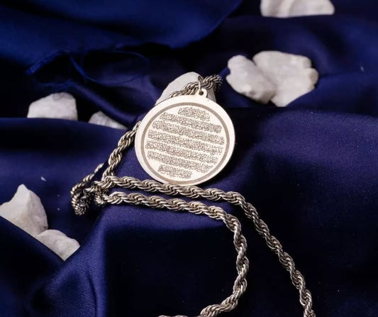 Silver Ayat ul Kursi pendant with intricate calligraphy on a twisted chain against dark blue fabric